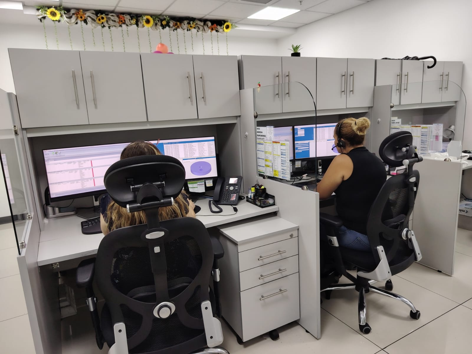 2 funcionarias del COAVIFMU de espaldas en sus lugares de trabajo con el equipo de cómputo para recibir llamadas